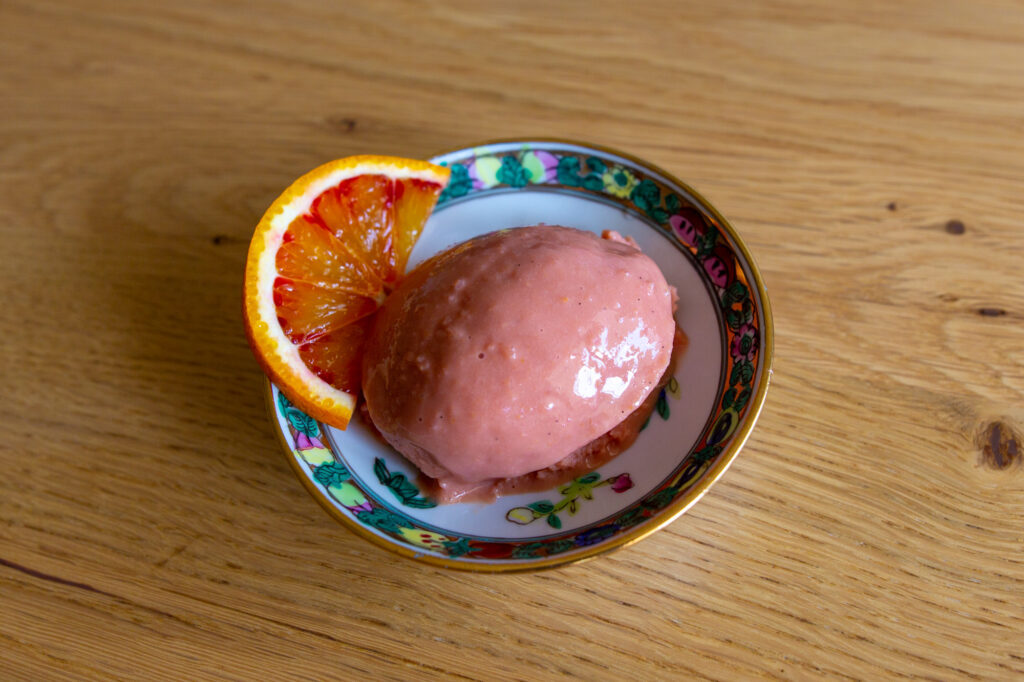 Vegan blood orange ice cream decorated with a slice of blood orange.