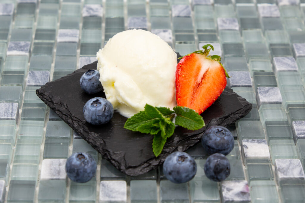 Joghurt-Eis in Kugelform mit frischen Heidelbeeren und Erdbeere arrangiert.