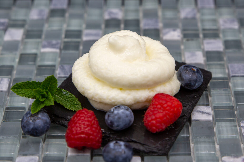 Joghurt-Eis mit einer Spritztülle in Kringelform gespritzt, arrangiert mit HImbeeren und Heidelbeeren.