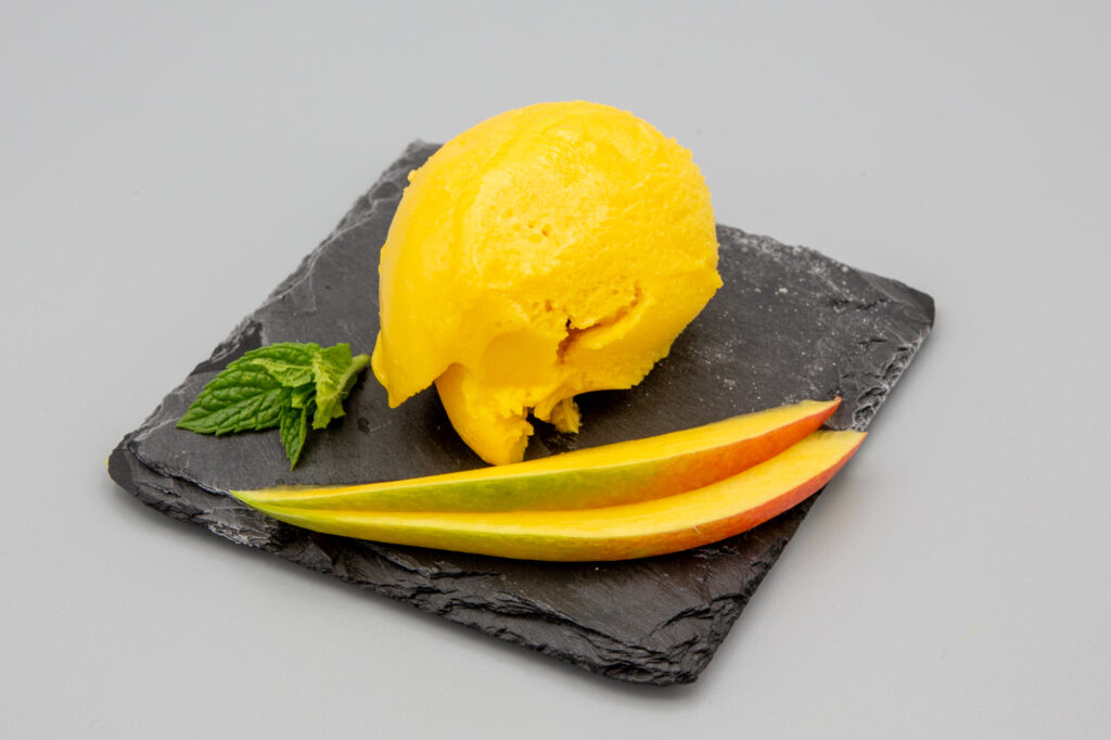 Fruchtiges Mango-Sorbet mit Mangospalten dekoriert.