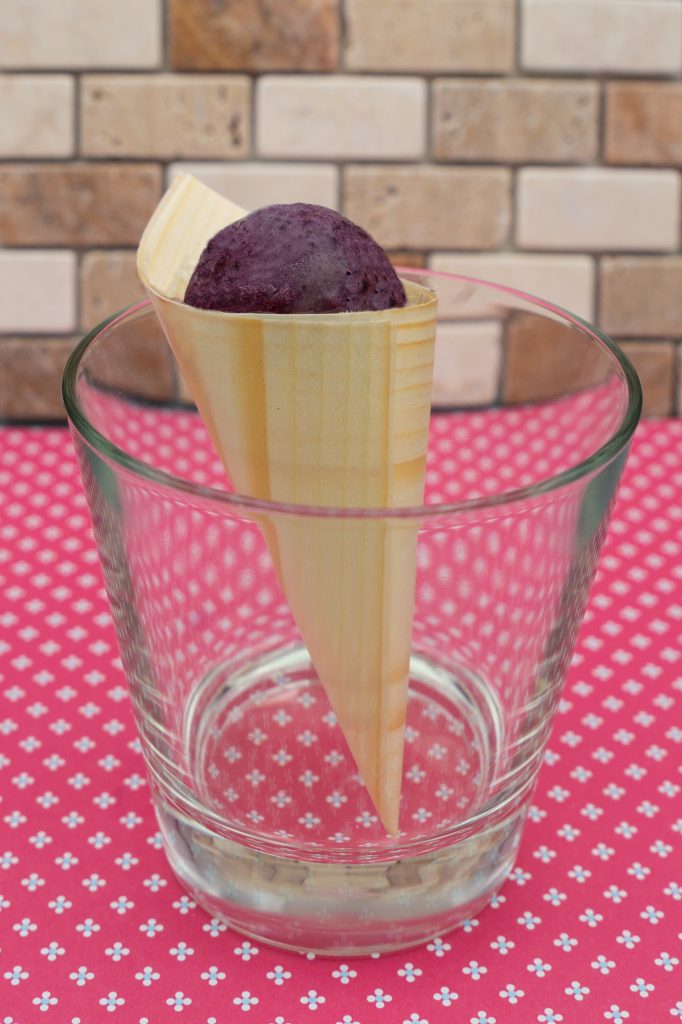 A scoop of dark purple cassis ice cream in a wooden horn.