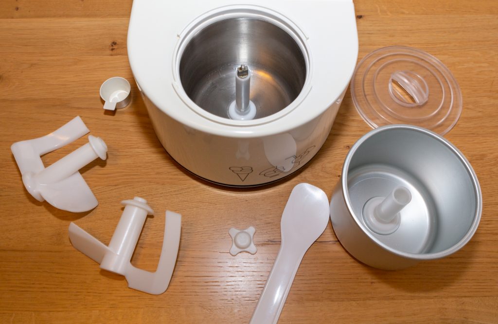 Nemox Gelatissimo with accessories: measuring cup, two stirrers, the fixing screw for the stirrer, ice spatula, aluminium container and lid (from left to right)