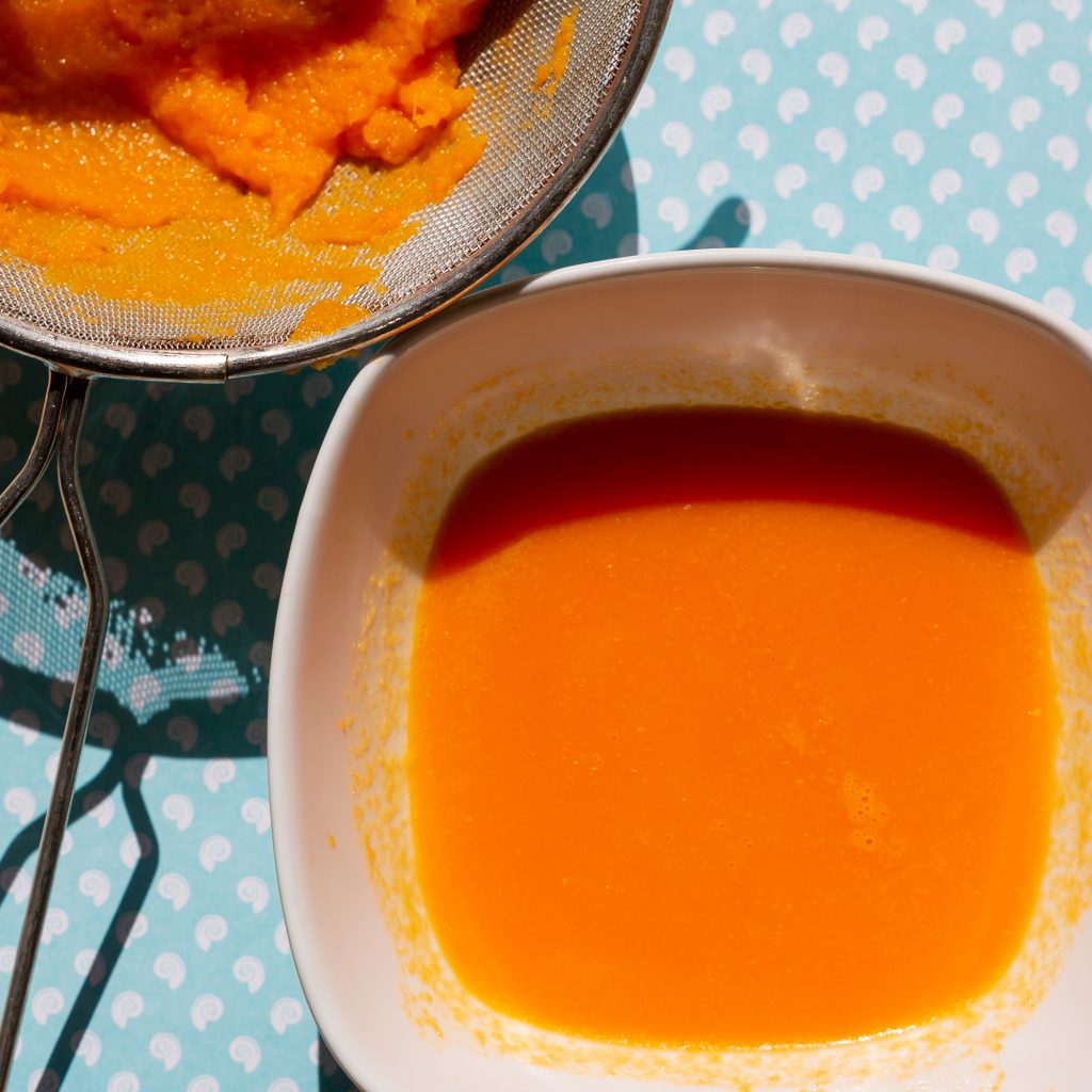 Durch ein Sieb werden die festen Anteile aus der Karotten-Orangen-Eismasse herausgefiltert.