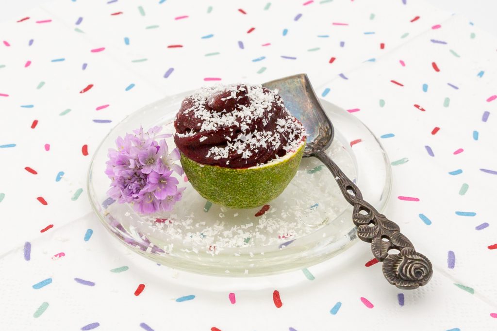 Heidelbeer-Eis Veganes Heidelbeer-Eis in Limettenschale arrangiert und bestreut mit Kokosraspel.