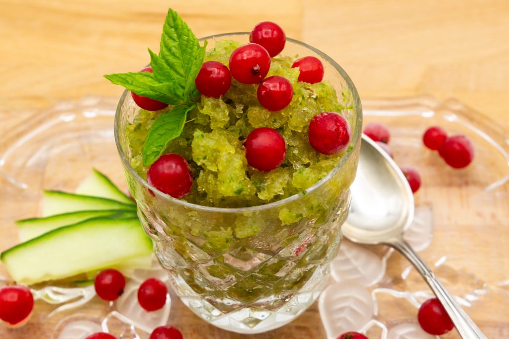 Gurken-Eis als Granita mit Johannisbeeren, Minze und Gurke dekoriert.