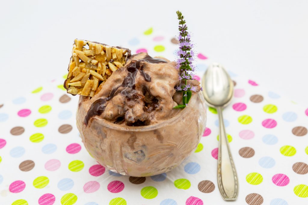 Nougat-Eis Cremiges Nougat-Eis serviert mit Schokoladen-Sauce und Nussplättchen.