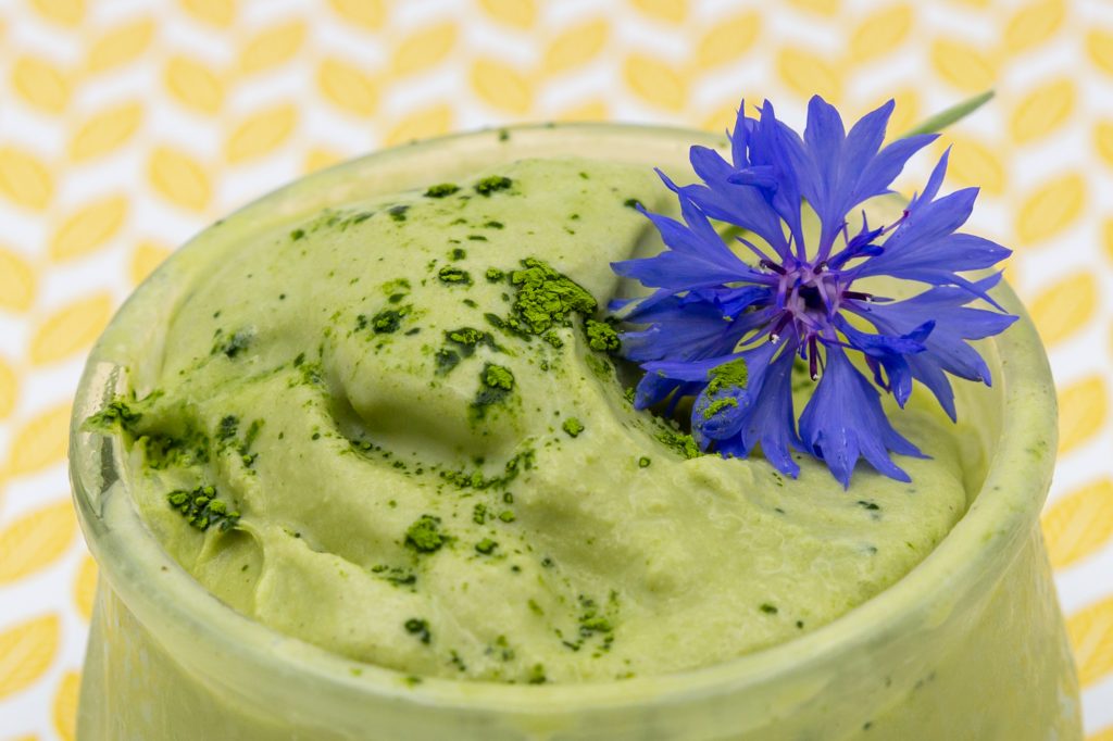 Cremiges Matcha-Eis bepudert mit Matcha-Pulver und dekoriert mit einer Kornblume.