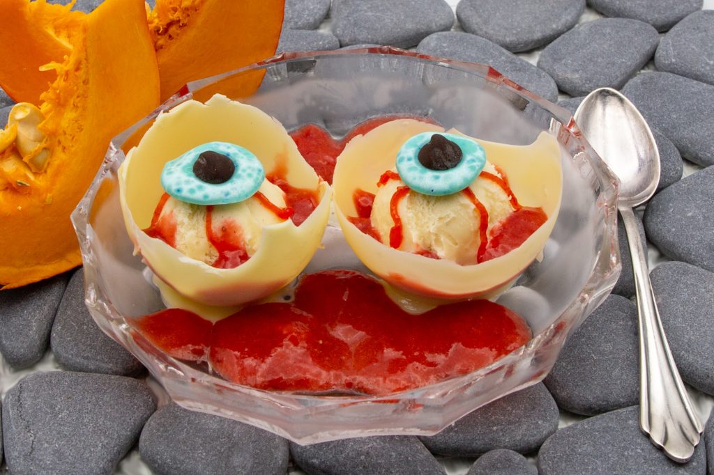 Gruselige Augäpfel aus Vanille-Eis mit Erdbeersauce als Nachtisch zu Halloween.