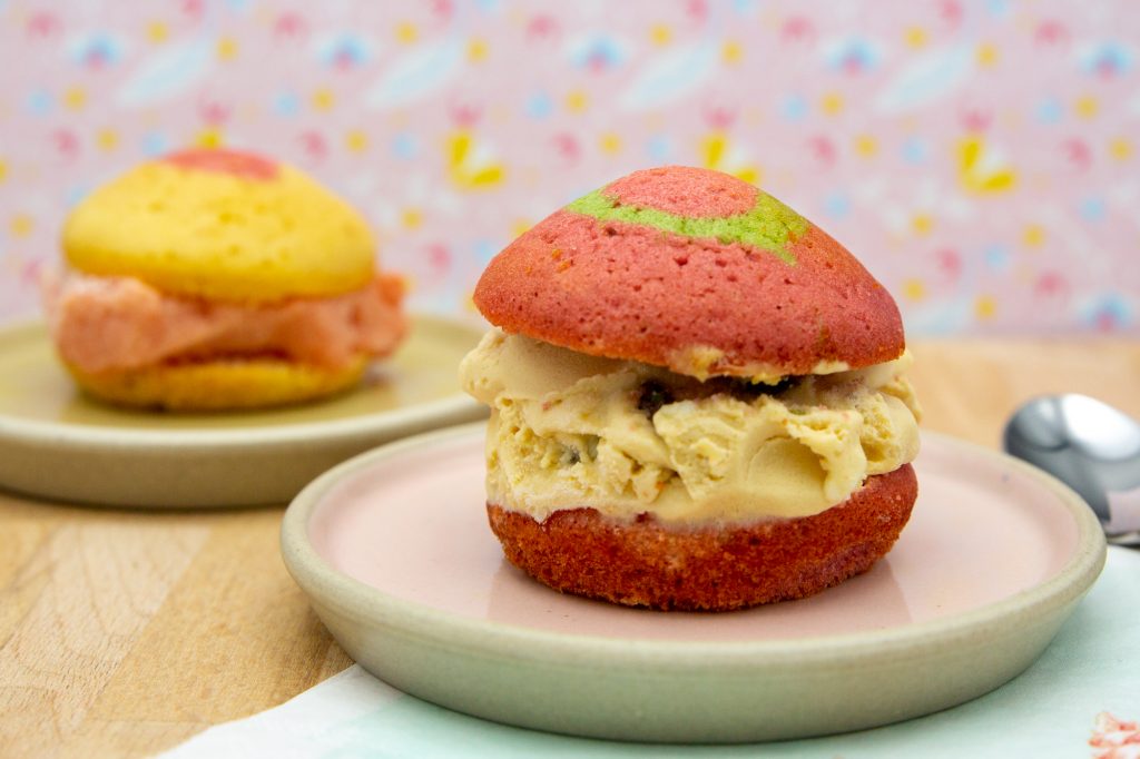 Ice cream cake with Malaga ice cream and watermelon ice cream in the background. The sponge cake is coloured with food colouring and baked in muffin tins.