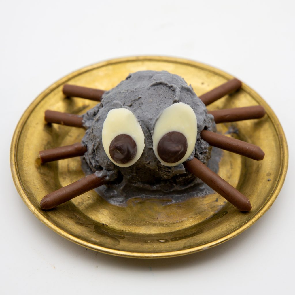 Halloweendessert Die fertig Spinne mit Beinen aus Mikadostäbchen und Augen aus weißer und dunkler Schokolade.