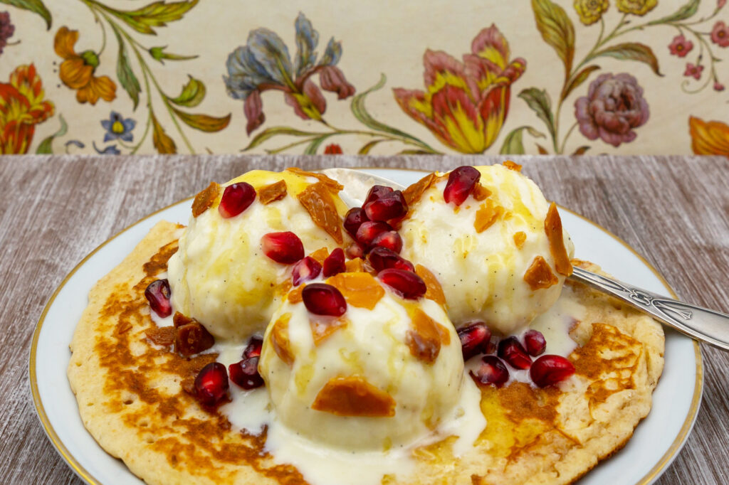 Creamy cashew ice cream on pancake with caramelized nuts, honey and pomegranate seeds.