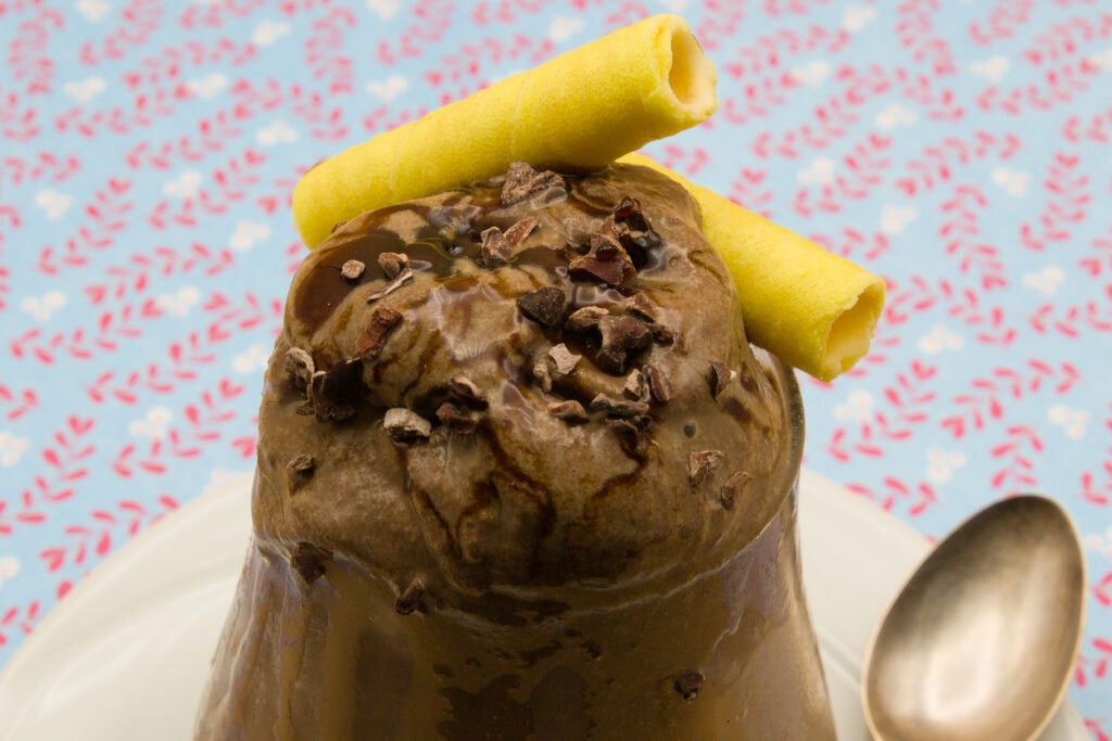 Eisbecher mit selbst gemachten Schokoladen-Eis und Schokoladen-Sauce. Dazu Kakaosplitter und Waffelröllchen.
