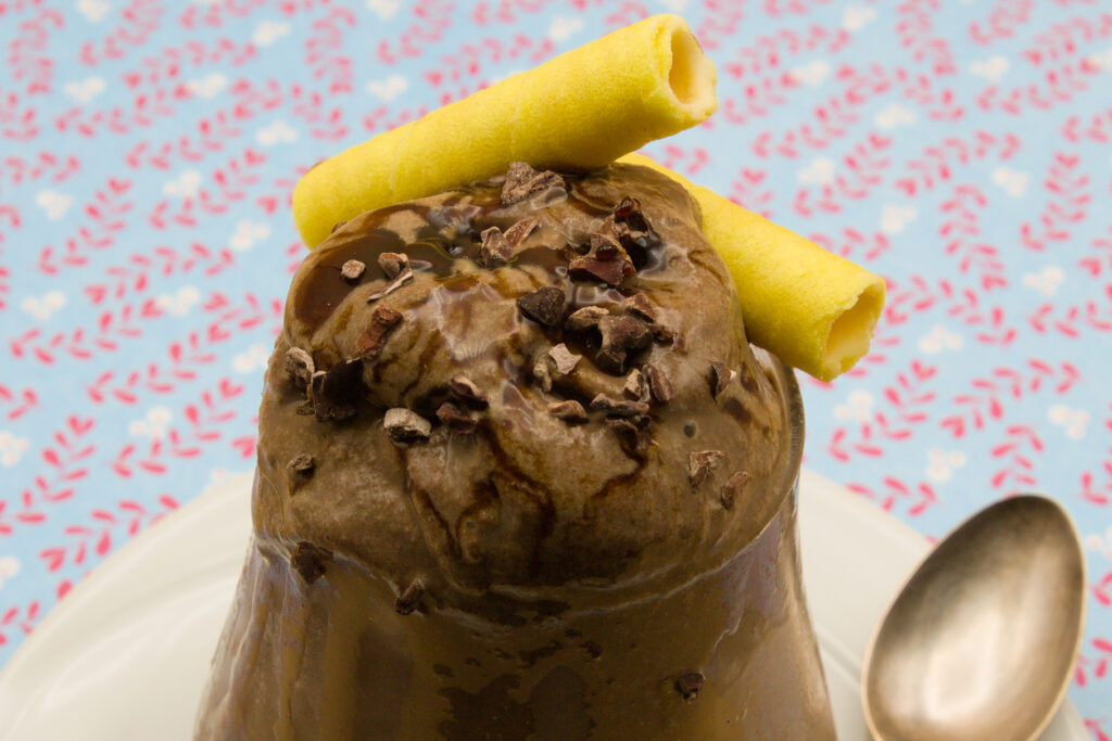 Schokoladen-Eis Eisbecher mit selbst gemachten Schokoladen-Eis und Schokoladen-Sauce. Dazu Kakaosplitter und Waffelröllchen.