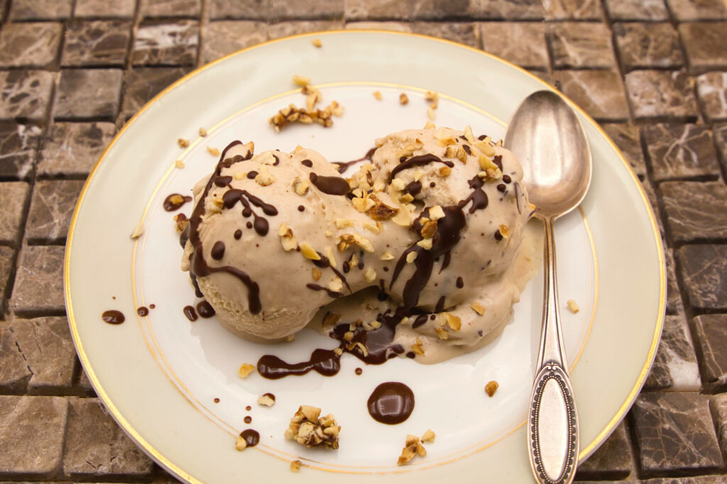 Creamy hazelnut ice cream decorated with liquid chocolate and roasted hazelnuts.
