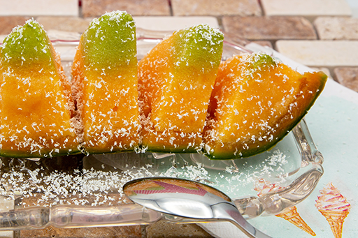 Melonen-Sorbet Melonen-Eis in der Melonenschale serviert. In der Mitte befindet sich Ananas-Minze-Sorbet. Die weißen Schokoladenraspel sehen fast wie Schnee aus.