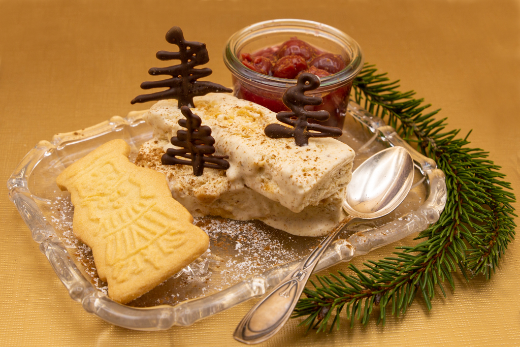 Weihnachtliches Spekulatius-Parfait mit heißen Kirschen und dekoriert mit Schoko-Weihnachtsbäumen.