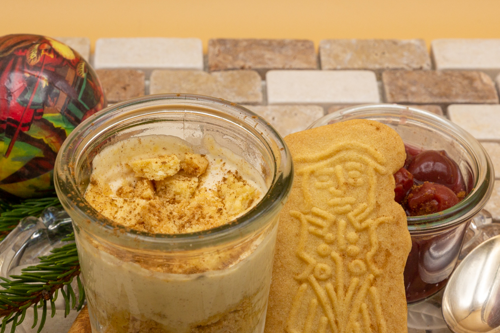 Delicious speculaas parfait layered in a glass with cinnamon sprinkled on top and hot cherries on the side.
