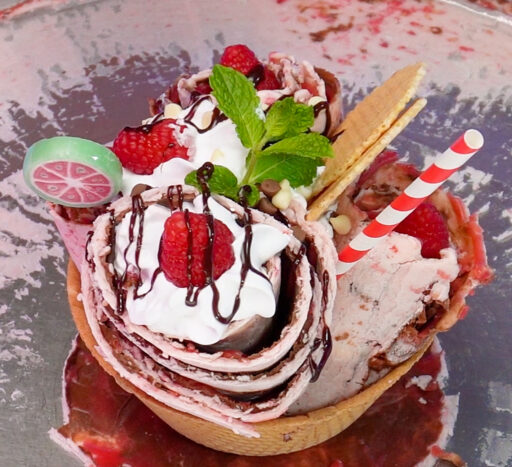 Rolled Ice Cream nicely arranged with raspberries in an ice cream cone. In the background you can see the ice cream slab.(Image courtesy of DJ Ice Rolls).